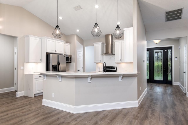 kitchen featuring appliances with stainless steel finishes, visible vents, wall chimney exhaust hood, and a kitchen bar