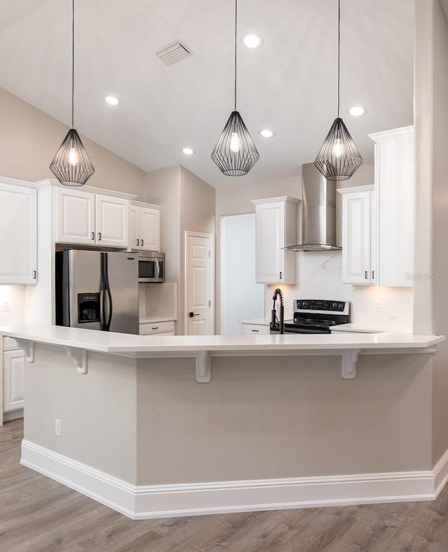 kitchen with appliances with stainless steel finishes, visible vents, wall chimney range hood, and a kitchen breakfast bar