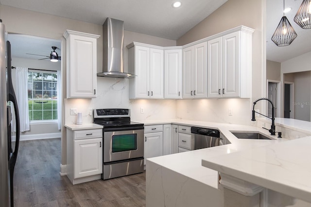 kitchen with lofted ceiling, a sink, white cabinets, appliances with stainless steel finishes, and wall chimney exhaust hood