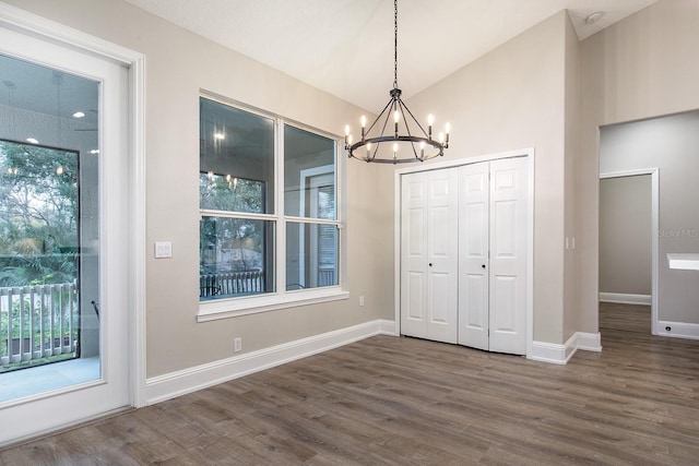 unfurnished dining area featuring lofted ceiling, dark wood-style flooring, baseboards, and an inviting chandelier