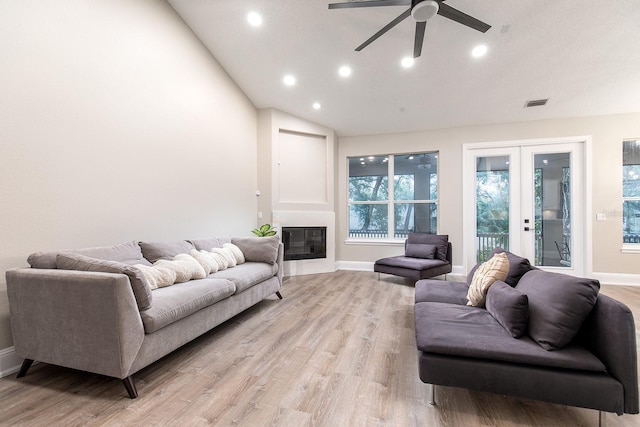 living room with visible vents, light wood-style floors, vaulted ceiling, french doors, and a glass covered fireplace