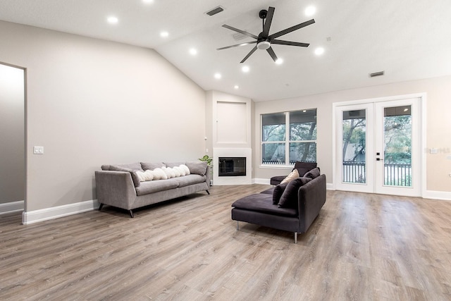 living area with a glass covered fireplace, french doors, visible vents, and vaulted ceiling