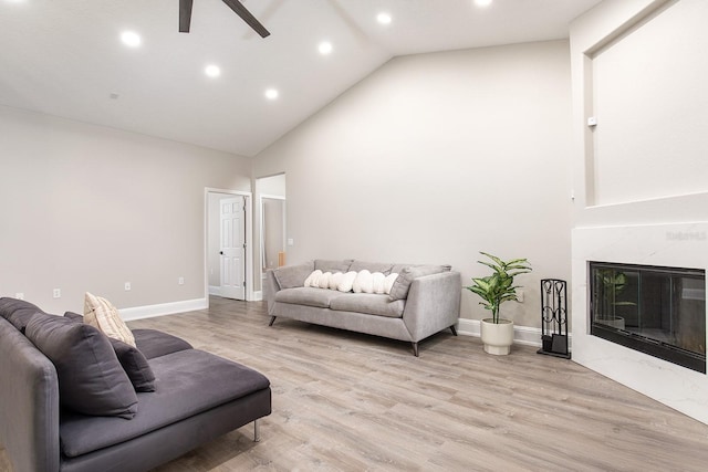 living area featuring high vaulted ceiling, light wood finished floors, a fireplace, and baseboards