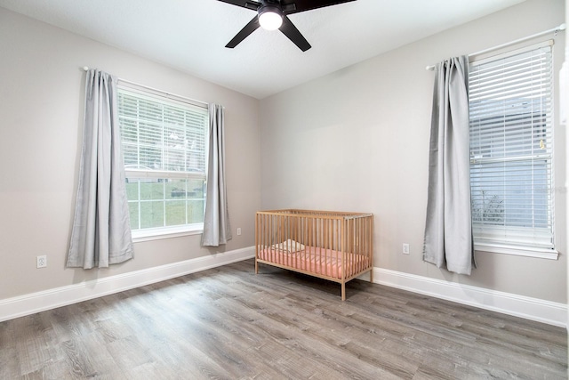 bedroom with a nursery area, wood finished floors, a ceiling fan, and baseboards