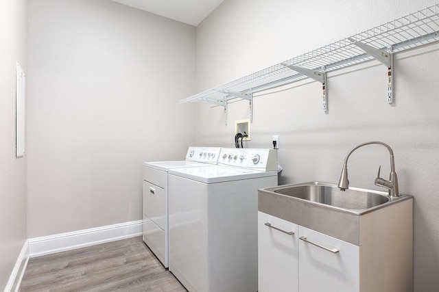 clothes washing area featuring light wood finished floors, washing machine and clothes dryer, cabinet space, a sink, and baseboards