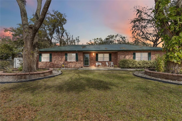 ranch-style house with fence, metal roof, a lawn, and brick siding