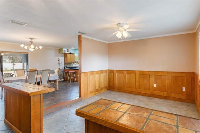 kitchen featuring visible vents, wainscoting, tile counters, brown cabinetry, and crown molding