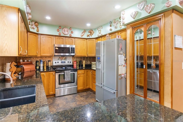 kitchen featuring appliances with stainless steel finishes, brown cabinets, dark stone countertops, a sink, and backsplash