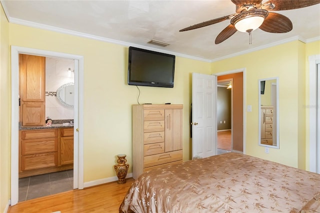 bedroom with connected bathroom, visible vents, baseboards, ornamental molding, and light wood finished floors