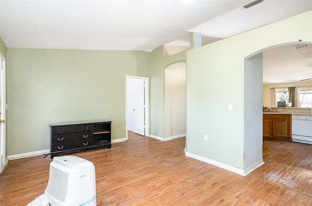 interior space featuring light wood-style flooring, arched walkways, vaulted ceiling, and baseboards