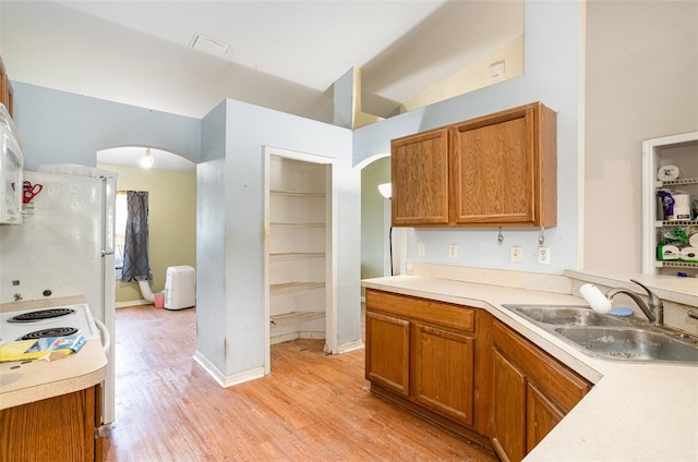 kitchen featuring arched walkways, brown cabinets, light wood-style flooring, a sink, and white appliances