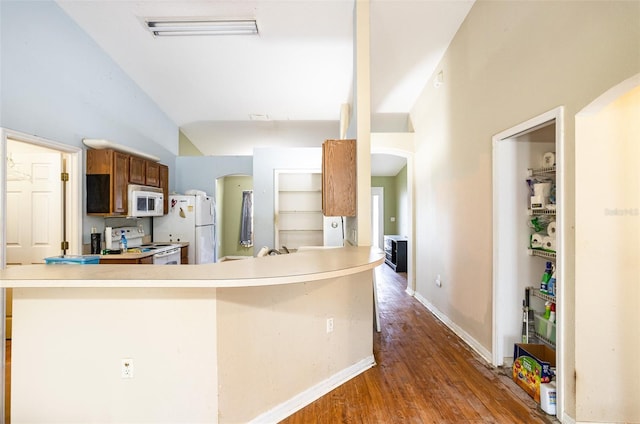 kitchen featuring dark wood-style floors, arched walkways, light countertops, white appliances, and baseboards