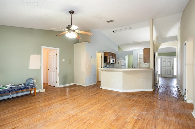 kitchen with white appliances, light wood finished floors, visible vents, arched walkways, and vaulted ceiling