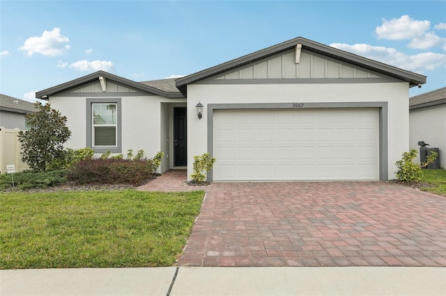 ranch-style home featuring an attached garage, decorative driveway, a front yard, board and batten siding, and stucco siding