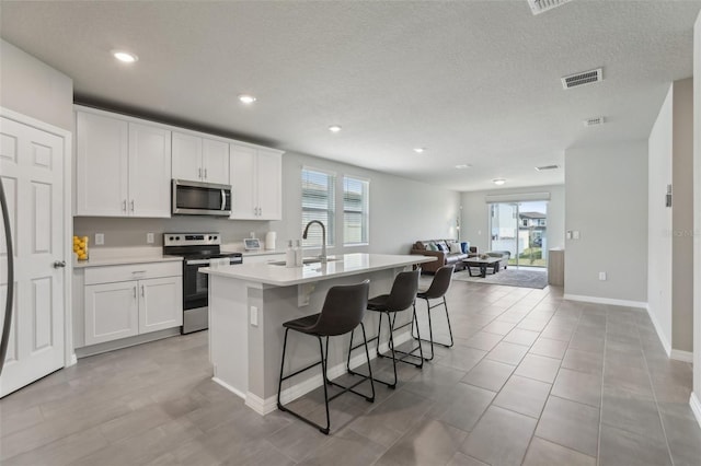 kitchen featuring stainless steel appliances, visible vents, white cabinets, light countertops, and a center island with sink