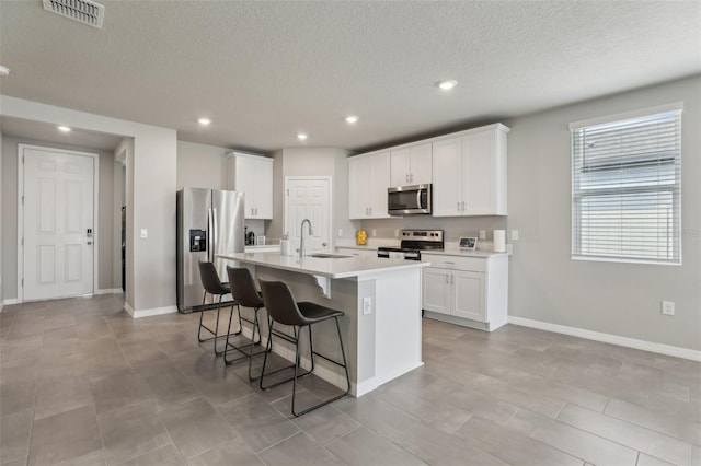 kitchen featuring a center island with sink, stainless steel appliances, light countertops, white cabinets, and a sink