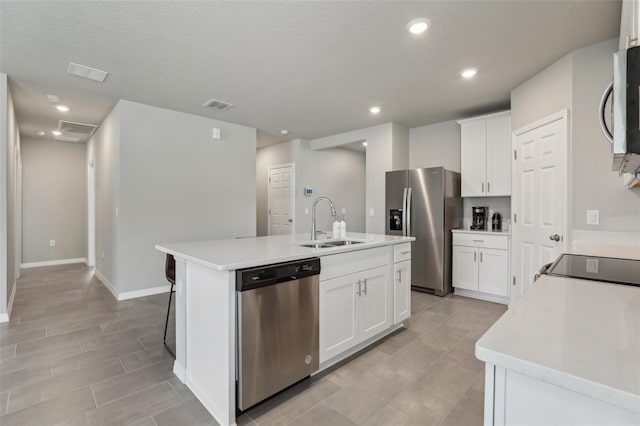 kitchen featuring white cabinets, appliances with stainless steel finishes, a kitchen island with sink, light countertops, and a sink