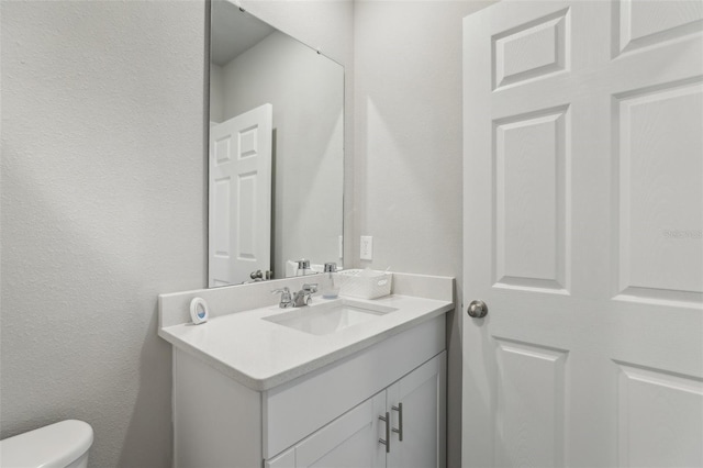 half bath featuring toilet, a textured wall, and vanity