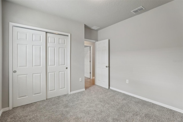 unfurnished bedroom featuring a textured ceiling, light colored carpet, visible vents, baseboards, and a closet