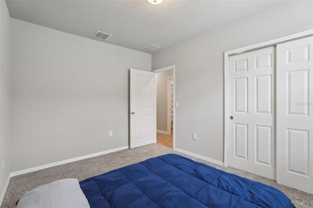 carpeted bedroom with baseboards, a textured ceiling, visible vents, and a closet