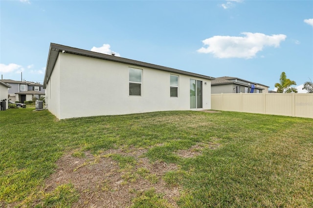 rear view of house featuring stucco siding, a lawn, central AC, and fence