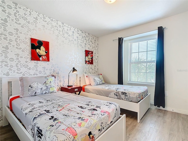 bedroom with wallpapered walls, an accent wall, baseboards, and wood finished floors