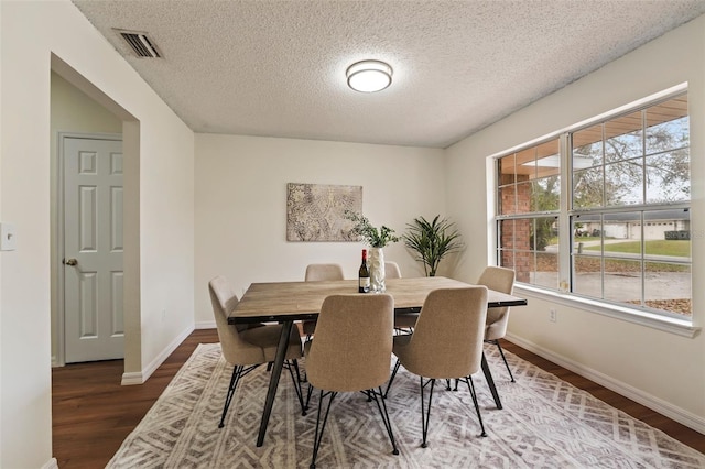 dining area with dark wood-style floors, visible vents, a textured ceiling, and baseboards