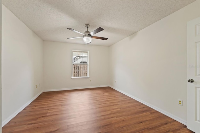 spare room with ceiling fan, a textured ceiling, baseboards, and wood finished floors