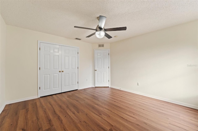 unfurnished bedroom with visible vents, a textured ceiling, baseboards, and wood finished floors