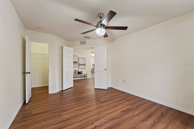 unfurnished bedroom with a spacious closet, a textured ceiling, visible vents, and dark wood-type flooring