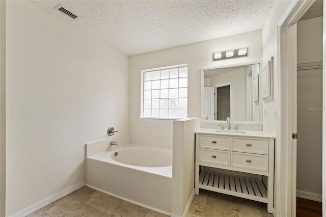 bathroom featuring baseboards, visible vents, a textured ceiling, vanity, and a bath