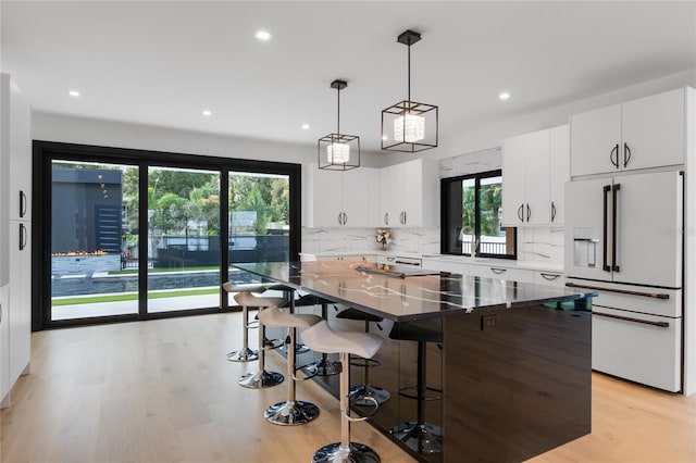 kitchen with light wood finished floors, tasteful backsplash, white refrigerator with ice dispenser, a kitchen bar, and white cabinetry