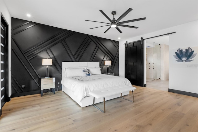 bedroom featuring ceiling fan, a barn door, a decorative wall, baseboards, and light wood-style floors