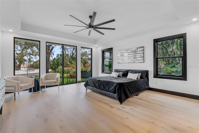 bedroom with a tray ceiling, light wood finished floors, recessed lighting, access to outside, and baseboards