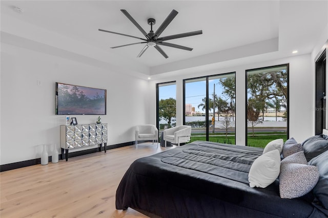 bedroom featuring light wood finished floors, a tray ceiling, baseboards, and a ceiling fan