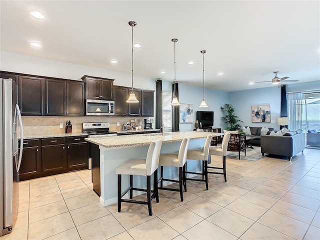 kitchen with appliances with stainless steel finishes, open floor plan, hanging light fixtures, and a center island with sink