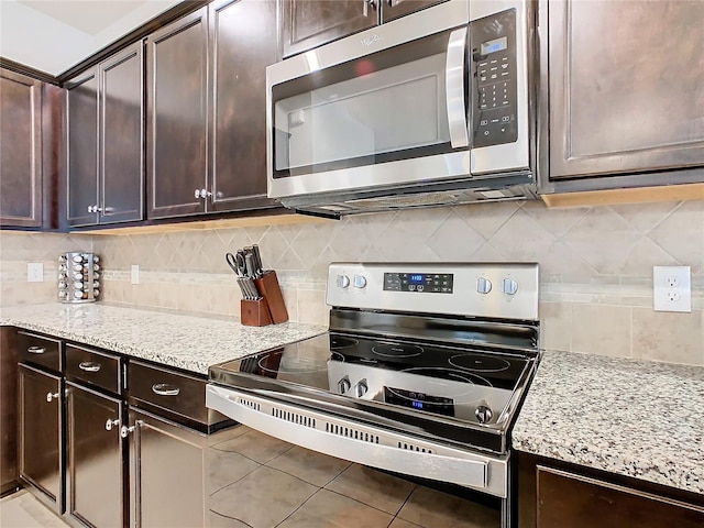 kitchen with light stone counters, stainless steel appliances, tasteful backsplash, dark brown cabinets, and tile patterned flooring