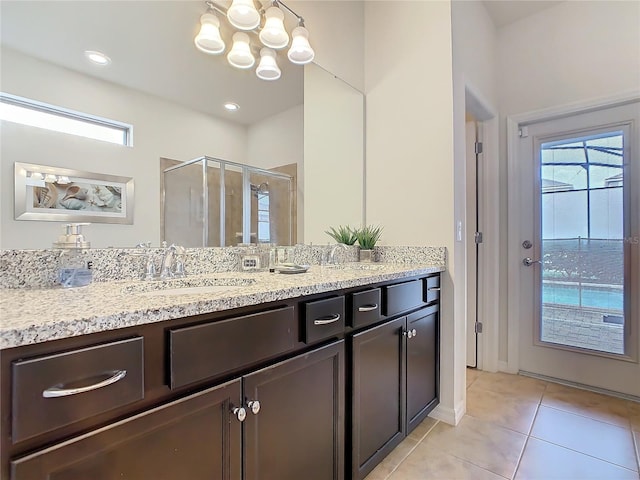 bathroom featuring a notable chandelier, double vanity, a stall shower, a sink, and tile patterned floors