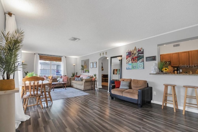 living area with arched walkways, a textured ceiling, dark wood-style floors, and visible vents