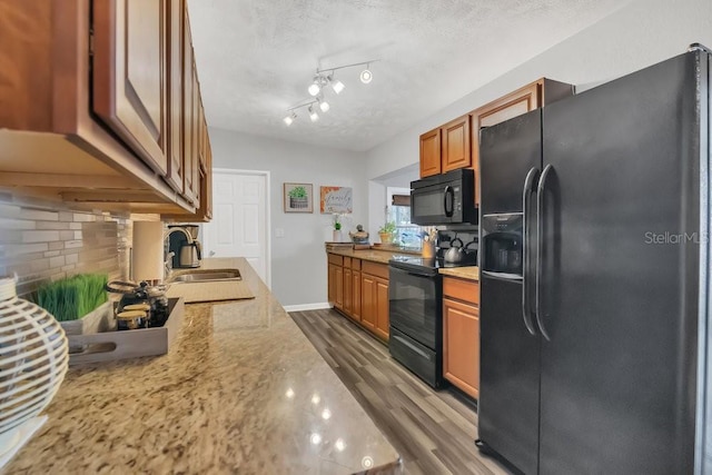 kitchen featuring dark wood-style floors, backsplash, a sink, light stone countertops, and black appliances