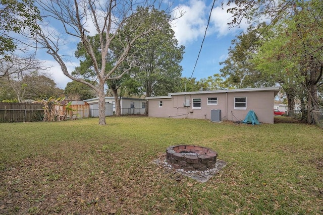 back of property with a fenced backyard, a lawn, a fire pit, and central air condition unit