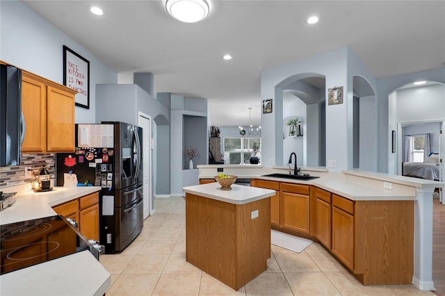 kitchen featuring light countertops, a peninsula, a sink, and a center island