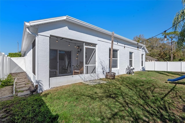 rear view of house with a sunroom, a fenced backyard, a lawn, and stucco siding