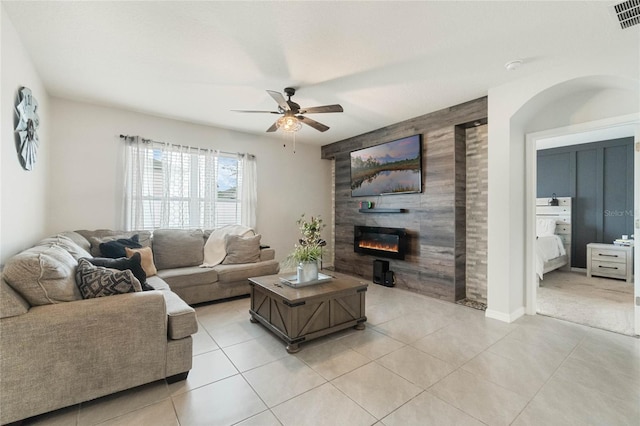 living room with ceiling fan, light tile patterned flooring, a large fireplace, an accent wall, and visible vents