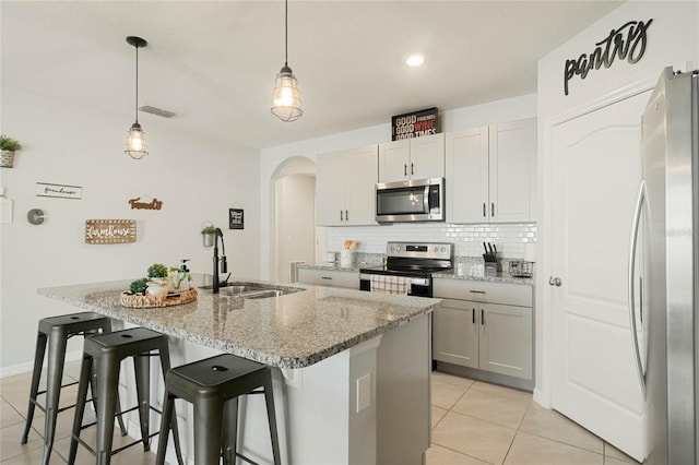 kitchen with hanging light fixtures, light stone countertops, a kitchen island with sink, stainless steel appliances, and a sink