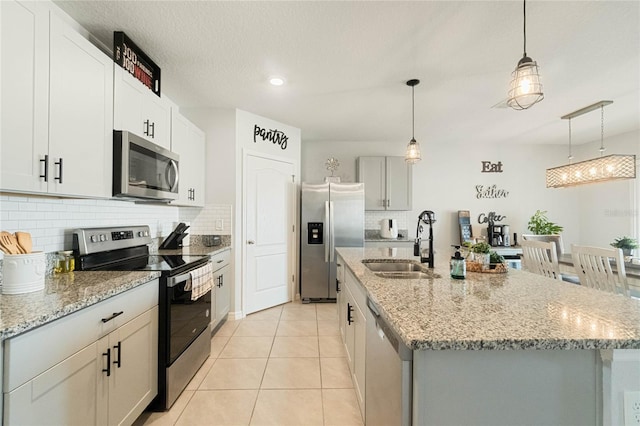 kitchen featuring appliances with stainless steel finishes, a kitchen island with sink, hanging light fixtures, and light stone counters