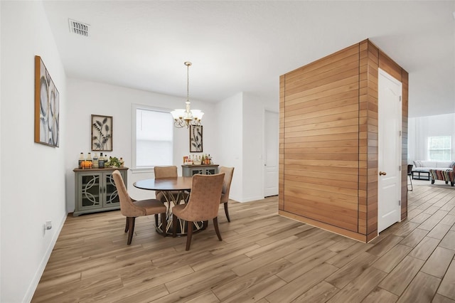 dining area with light wood finished floors, baseboards, visible vents, and a notable chandelier