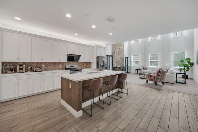 kitchen featuring light countertops, appliances with stainless steel finishes, an island with sink, and white cabinetry