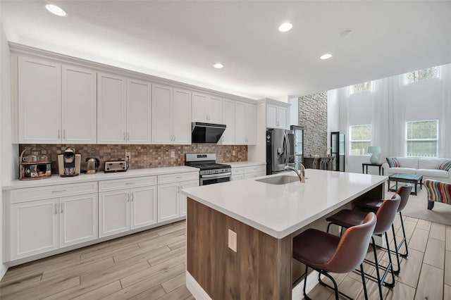 kitchen featuring stainless steel appliances, light countertops, a sink, and an island with sink