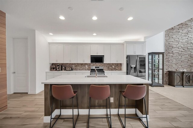 kitchen featuring stainless steel appliances, white cabinets, light countertops, backsplash, and a center island with sink